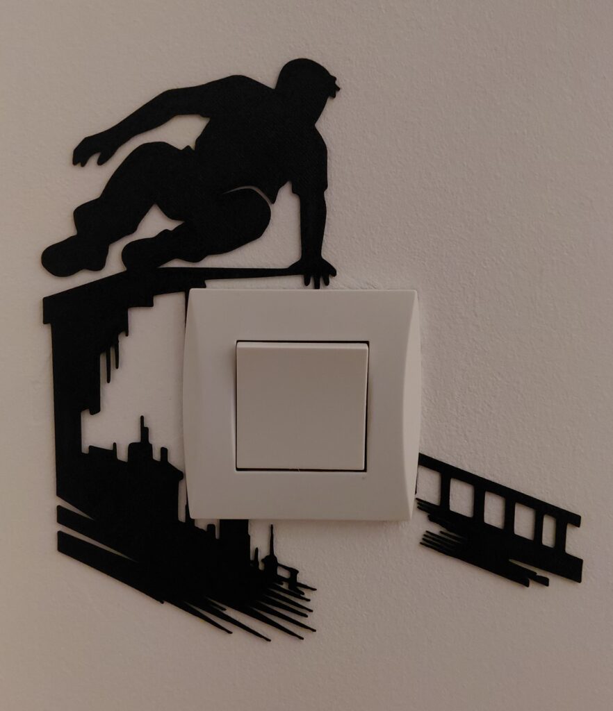 Plaque décorative noire à motif de parkour, montée derrière l’enjoliveur blanc d’un interrupteur